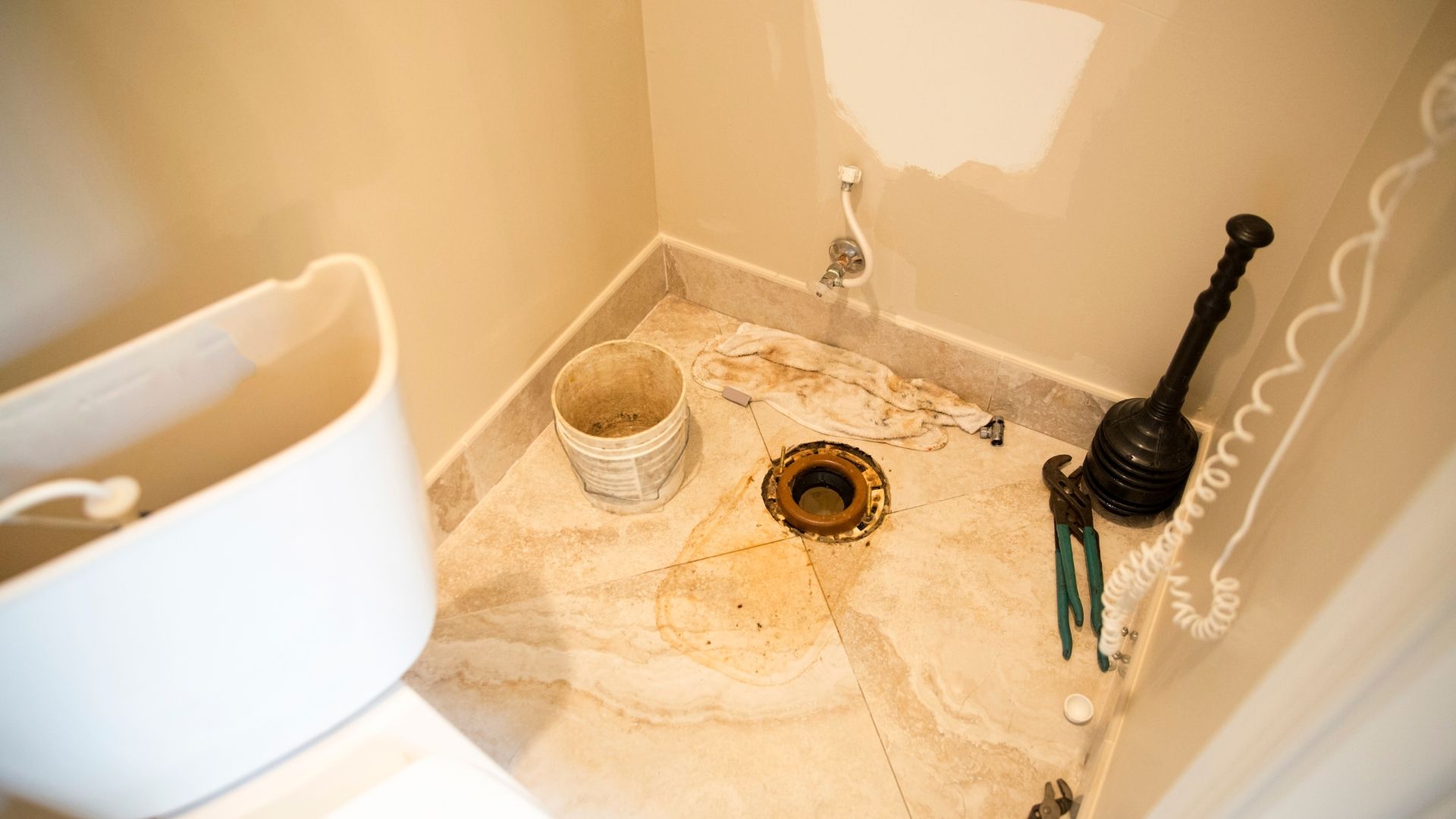 Toilet repair tools and plunger on a beige bathroom floor
